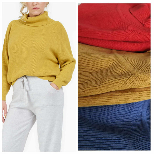 A woman wearing a yellow sweater and white pants stands next to a collage of colorful knitted sweaters.