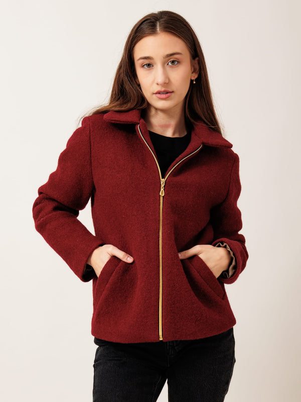 A young woman wearing a red coat with a zipper and standing against a plain background.