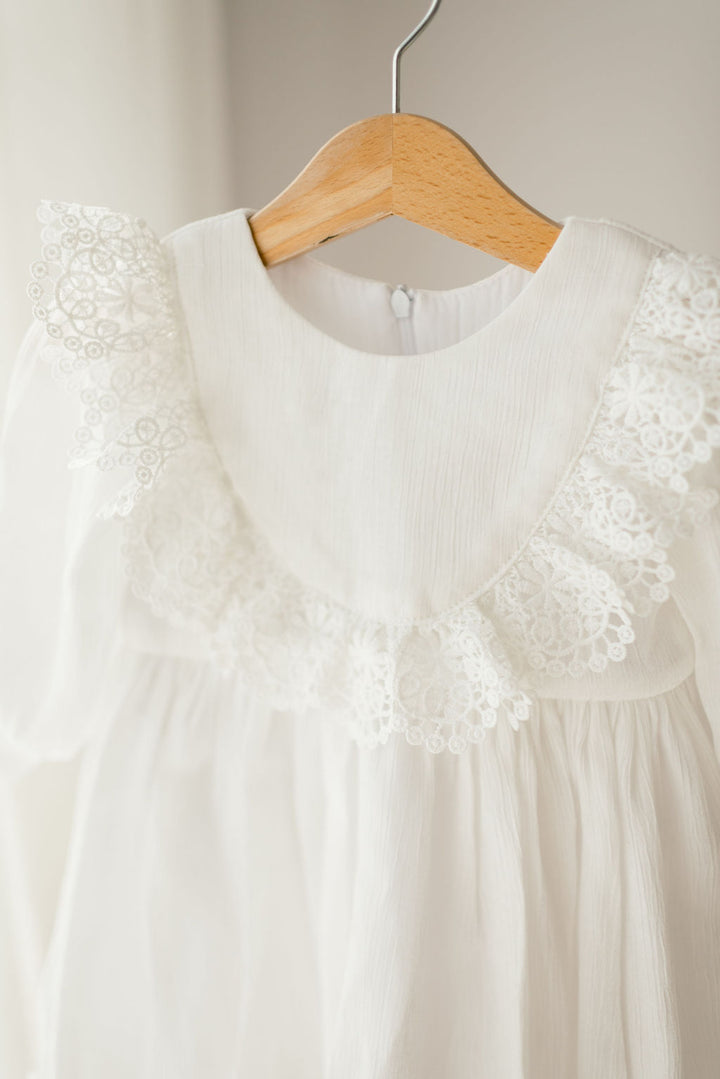 A white dress with lace trim hanging on a wooden hanger.