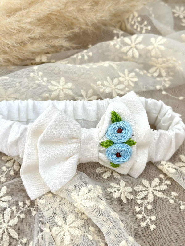 A white bow with blue flowers is displayed on a white lace background.