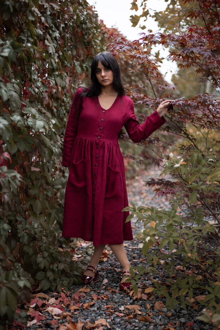 A woman in a red dress stands amidst a lush, leafy garden, surrounded by vibrant autumn foliage.