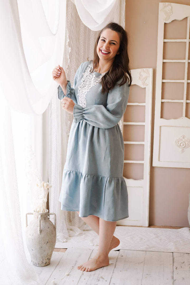a woman in a blue dress standing in front of a window