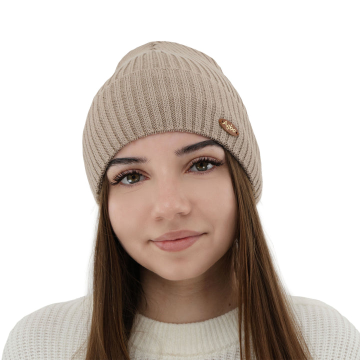 A young woman with long brown hair wearing a beige knit hat with a small logo on it, smiling at the camera.