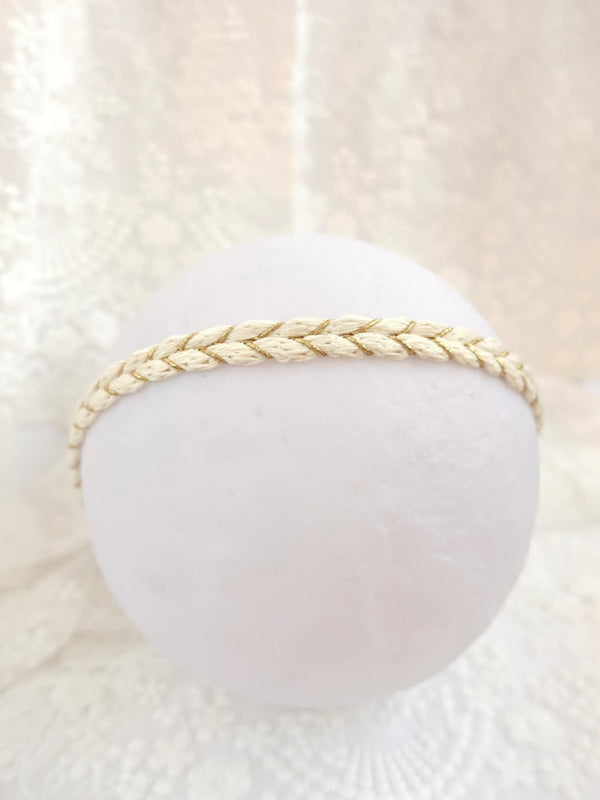 A white, round object with a braided strap or band around it, placed against a white lace background.