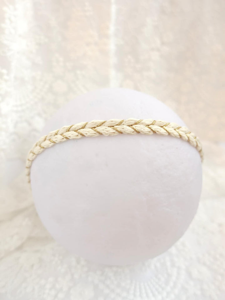 A white, round object with a braided strap or band around it, placed against a white lace background.