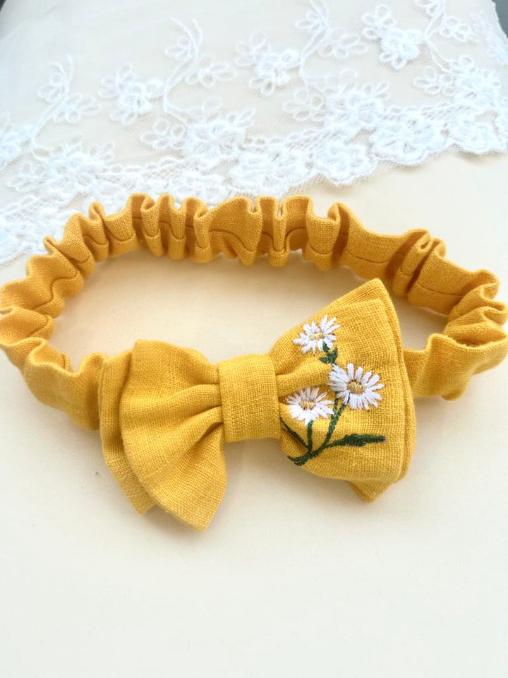 A yellow bow tie with white flowers on it, placed on a white surface.