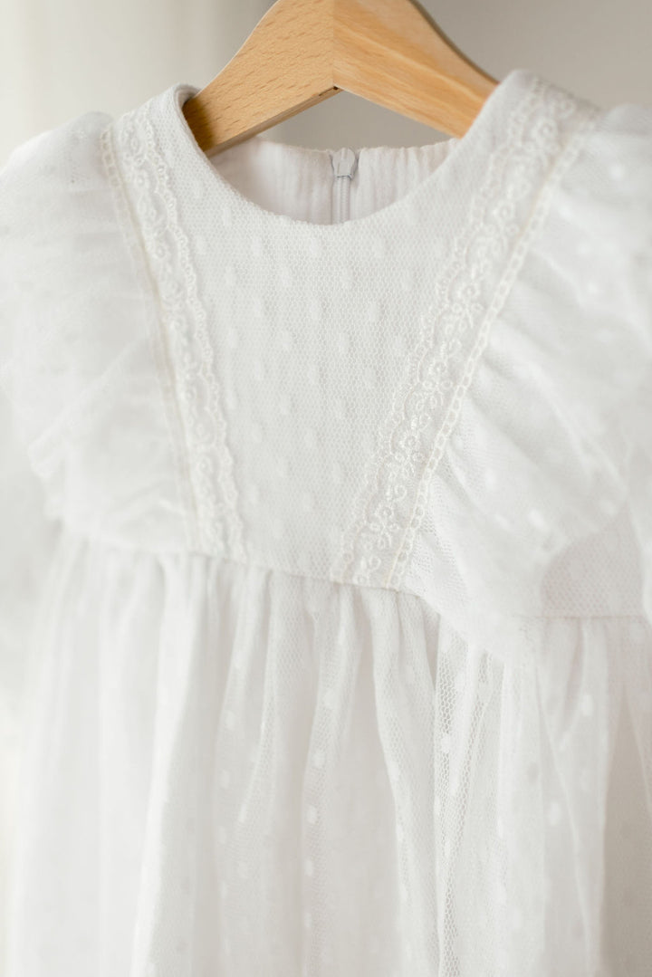 A white, ruffled dress with lace trim hanging on a wooden hanger.