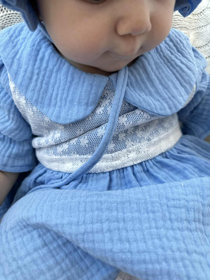 A close-up image of a baby wearing a blue dress with lace detailing.