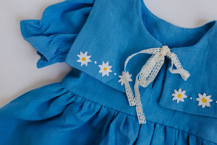 A blue dress with white daisy embroidery and a white lace bow.