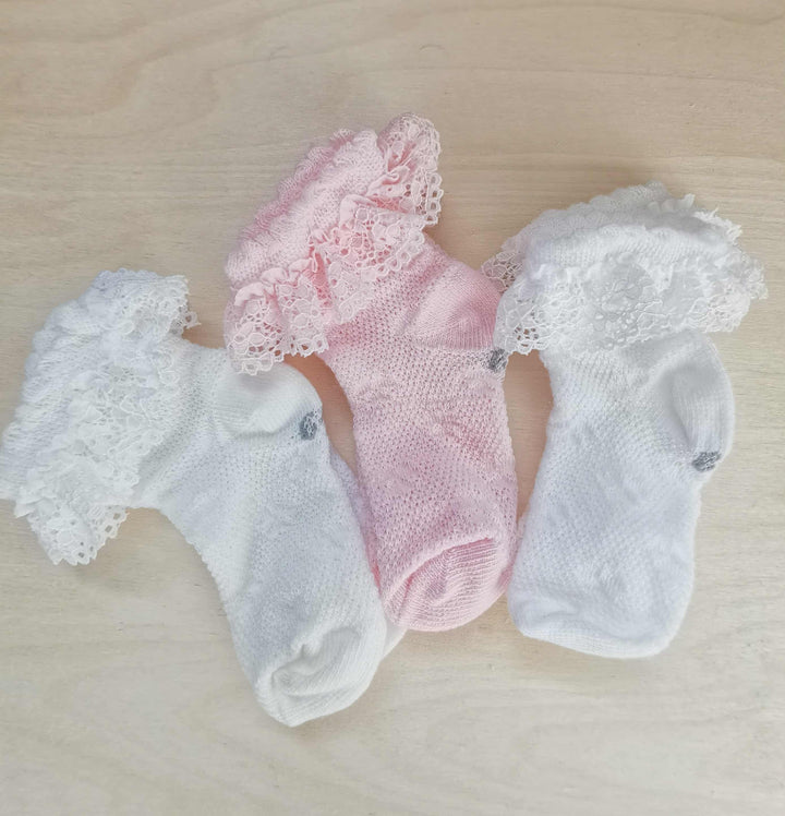 Three pairs of white lace socks with ruffled details are arranged on a wooden surface.