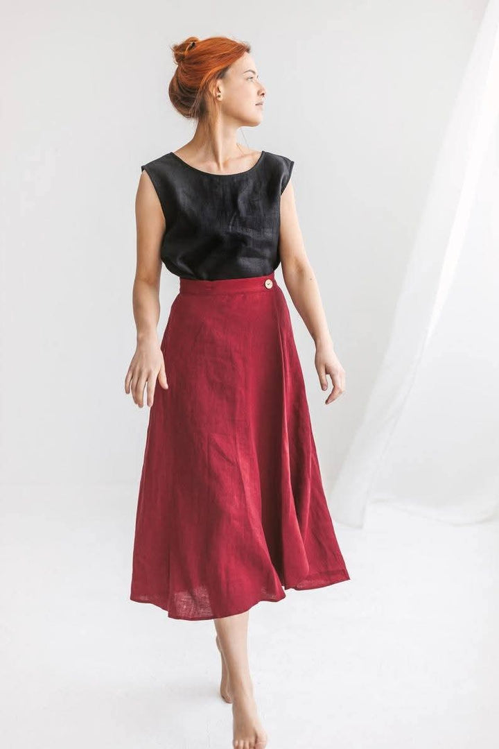 A woman with red hair wearing a black top and a red skirt stands against a white background.