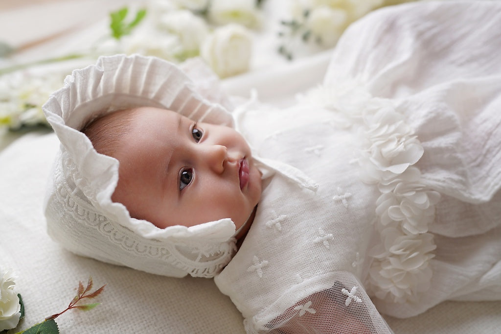 a baby in a white dress laying on a bed