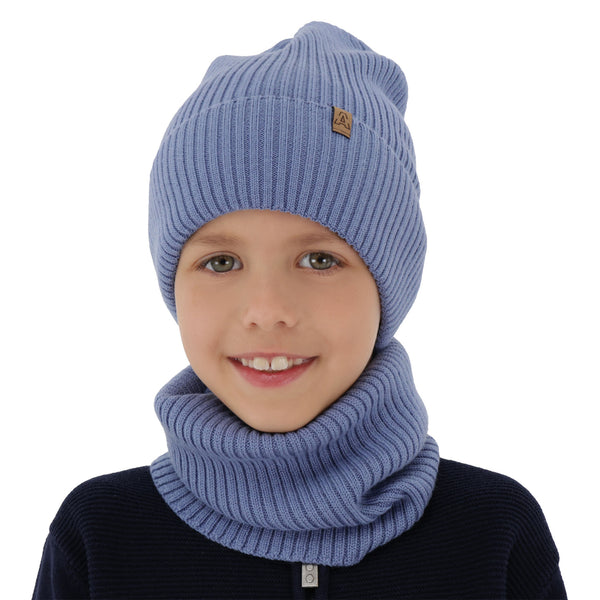 A young child wearing a blue knit hat and scarf, smiling at the camera.