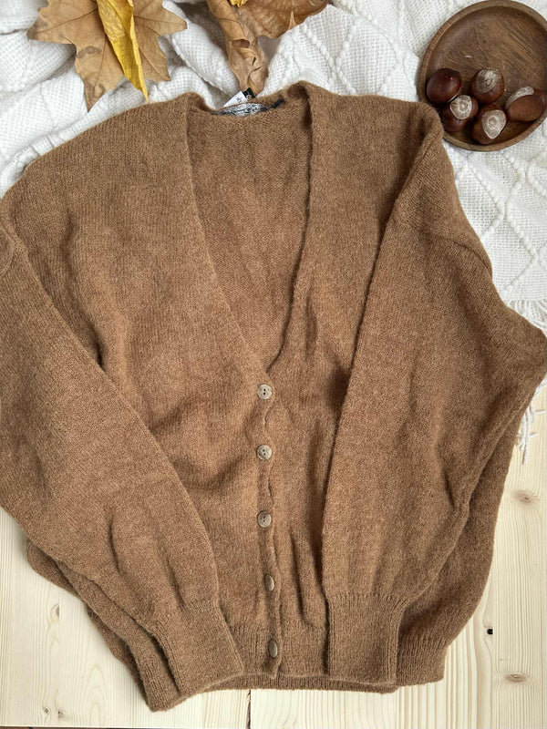 a brown cardigan with buttons laid out on a wooden surface, accompanied by a small bowl containing chestnuts.