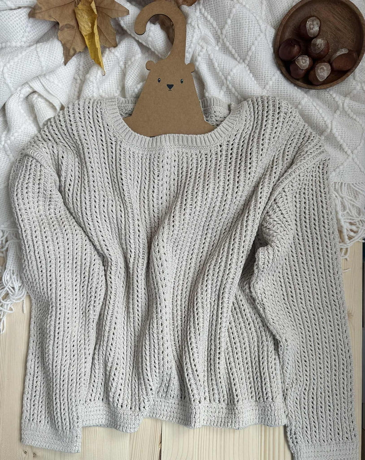 a cozy gray knitted sweater hanging on a wooden hanger, with a bowl of chestnuts placed nearby.