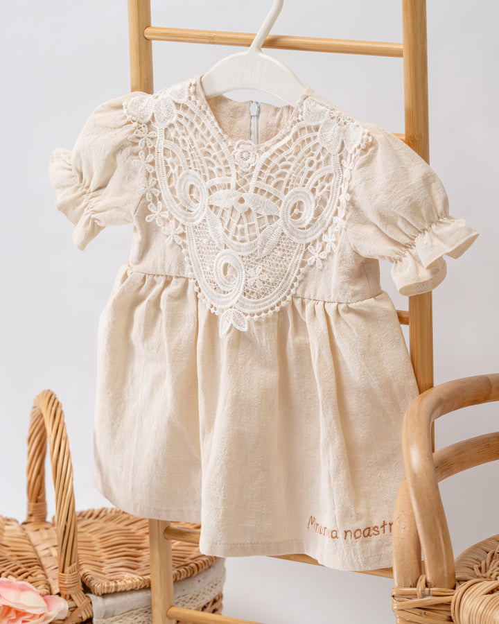 A white lace dress with a floral pattern is hanging on a wooden hanger.
