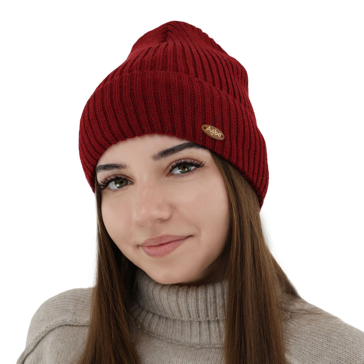 A young woman wearing a red knit hat with a gold logo on it, smiling at the camera.
