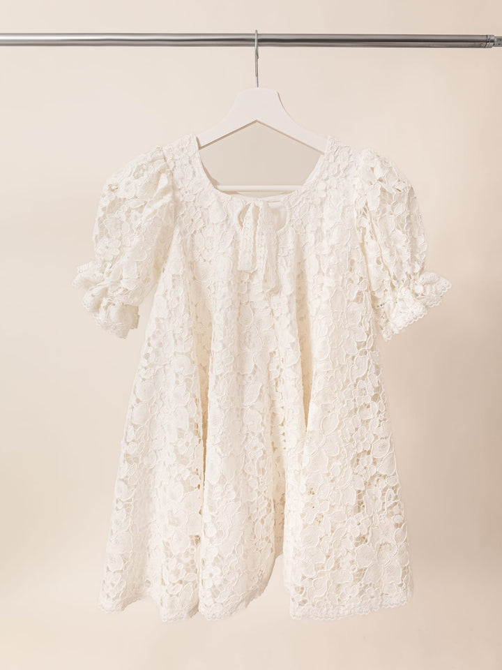 A white lace dress with puffed sleeves is hanging on a white hanger against a light background.