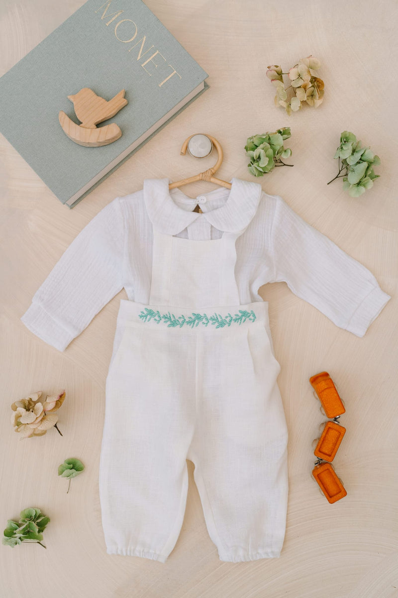a white onesie with green leaves, a wooden rocking horse, a book titled "MONET", and some flowers and orange keys on a light-colored surface.