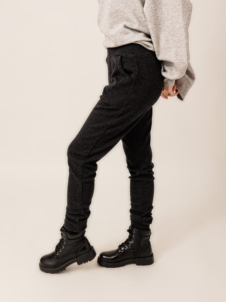 A person wearing a gray sweatshirt, black pants, and black boots stands with their hands in their pockets.