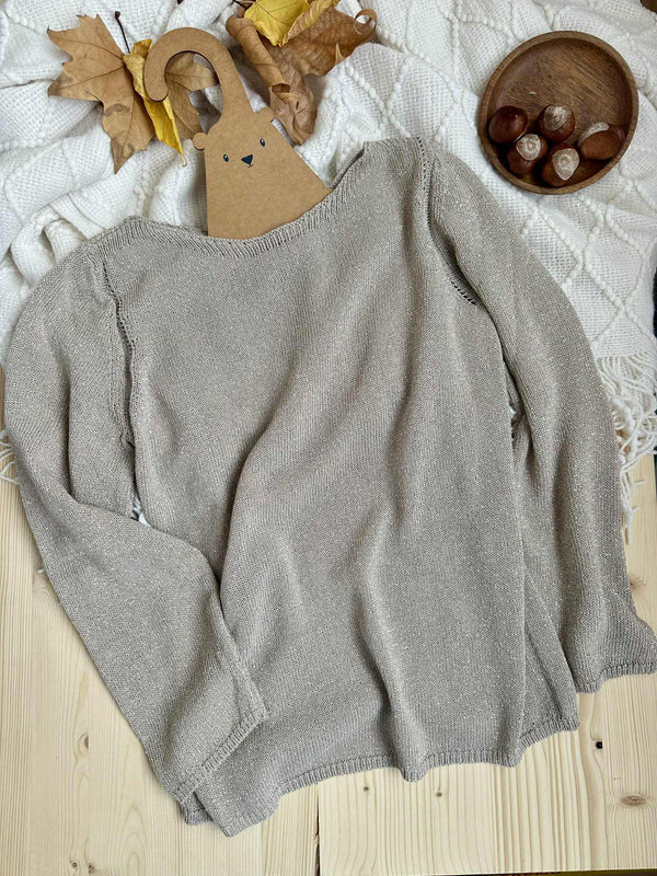 a gray sweater laid out on a wooden surface, with a wooden bowl containing brown objects placed to the right of the sweater.