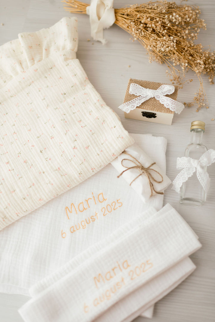 a collection of items, including a white cloth with a floral pattern, a small wooden box, a white ribbon, a white bow, and a small glass bottle. The items are arranged on a white surface, creating a visually appealing and organized composition.