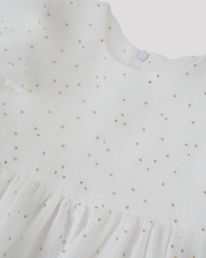 A close-up view of a white dress with gold polka dots, featuring a ruffled collar and a ruffled hem.