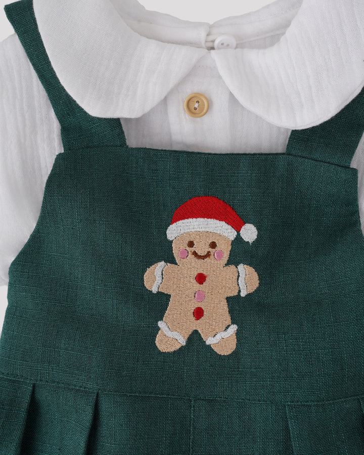 A green dress with a red and white gingerbread man embroidered on it, wearing a Santa hat.