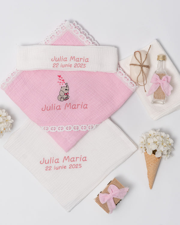 a pink towel with a name embroidered on it, a small gift box, a bottle, and some flowers.