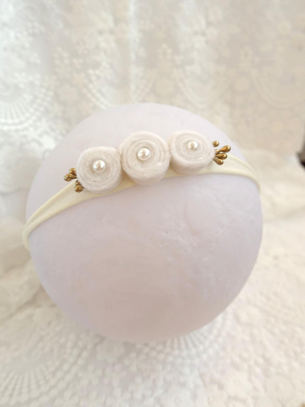 A white headband with three round beads on top, placed on a white lace background.