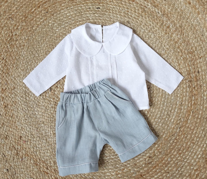 A white collared shirt and gray shorts are laid out on a woven mat.