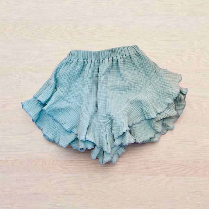 A pair of light blue ruffled shorts is displayed on a light pink background.