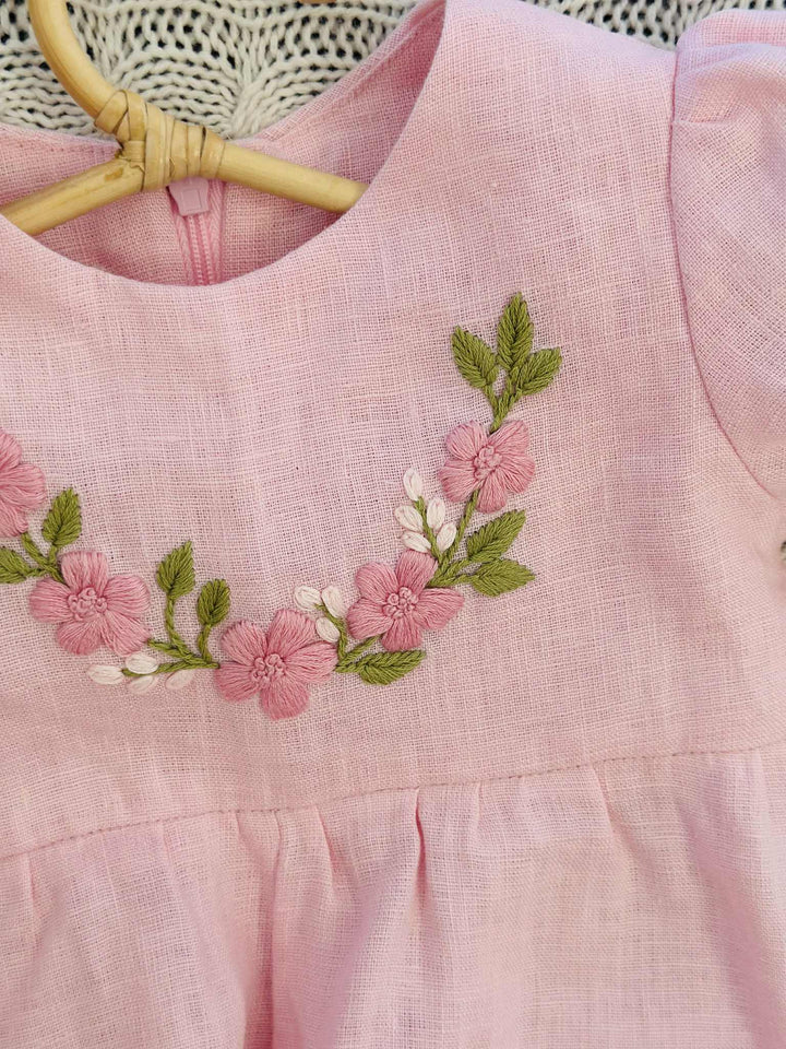 A close-up view of a pink dress with a floral embroidered design on the front.