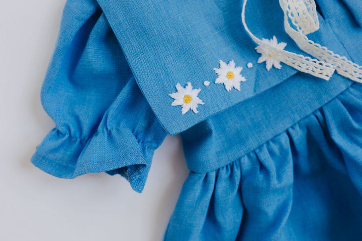 A blue dress with white daisy embroidered details, including three flowers on the front.
