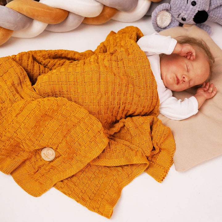A newborn baby is peacefully sleeping, wrapped in a cozy yellow blanket, with a stuffed animal nearby.