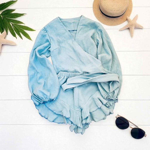 a light blue dress laid out on a white background, along with a straw hat and sunglasses.