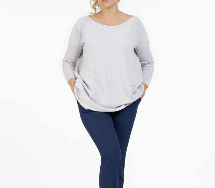 A woman wearing a gray sweater and navy blue pants stands against a white background.