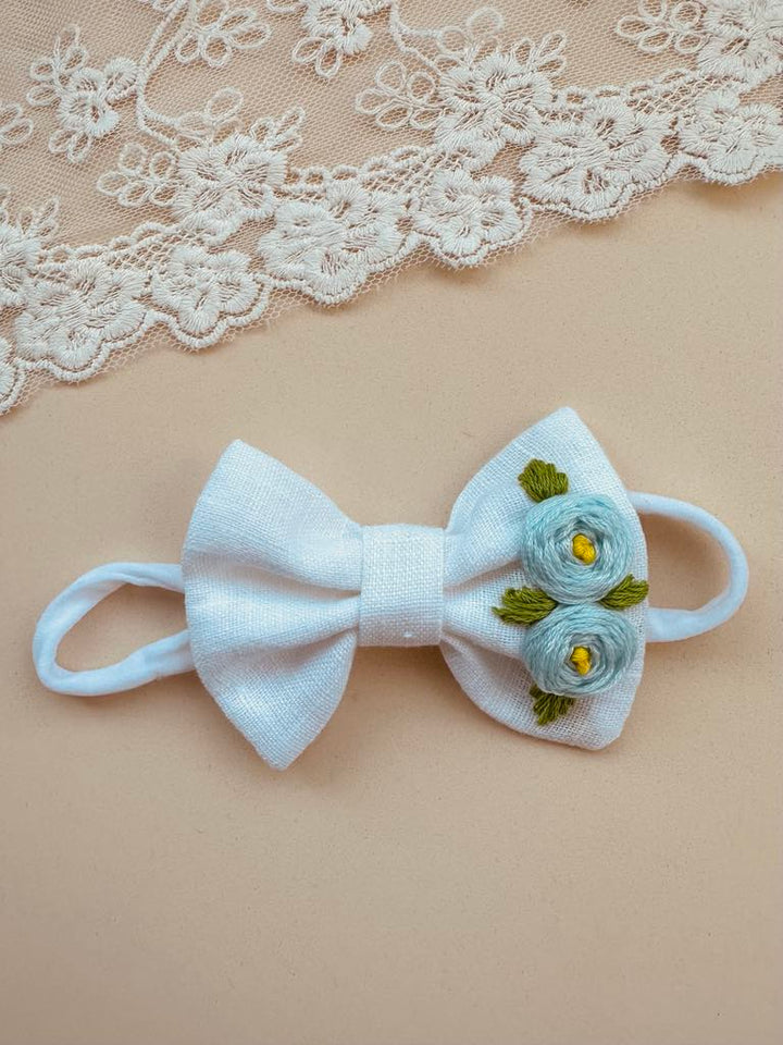 A white bow with blue flowers on it, placed on a beige background with a lace doily.