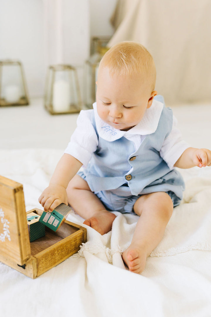 A baby sitting on a white blanket, playing with a wooden box.