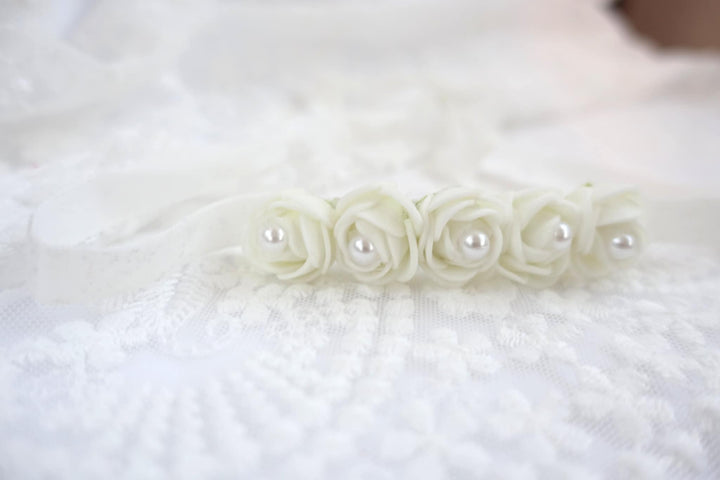 A delicate white flower arrangement with five petals and white pearls rests on a white lace background.