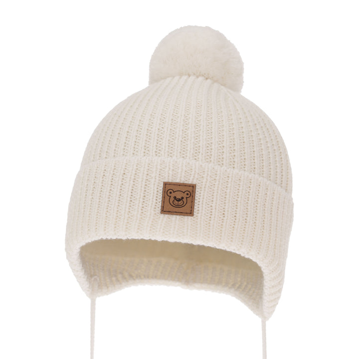 A white knit beanie with a pom pom on top, featuring a small brown patch with a bear face on the front.