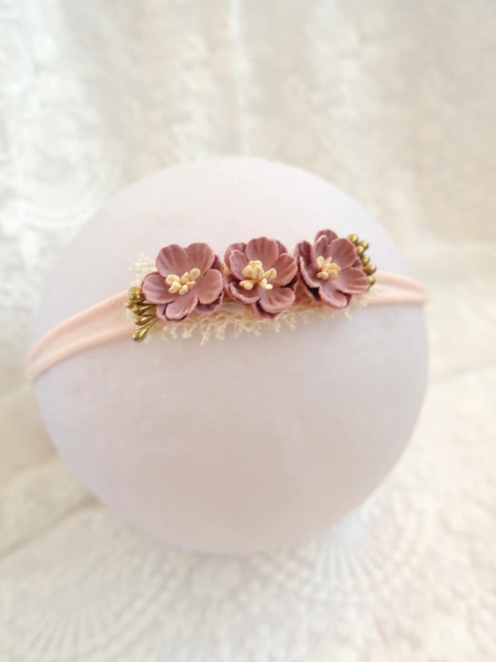 A white headband adorned with three pink flowers is displayed against a white background.