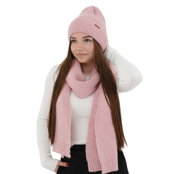 A woman wearing a pink knit hat and scarf, with long brown hair, posing against a white background.