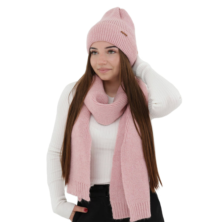 A woman wearing a pink knit hat and scarf, with long brown hair, posing against a white background.