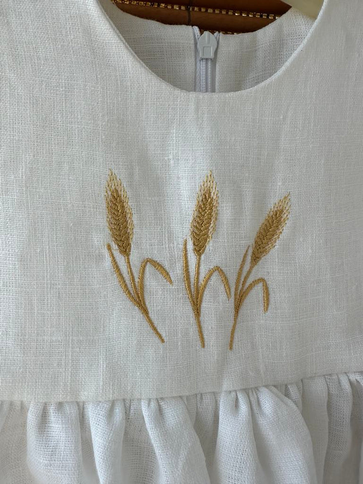 a close-up view of a white dress with a decorative embroidered design featuring three golden wheat stalks.
