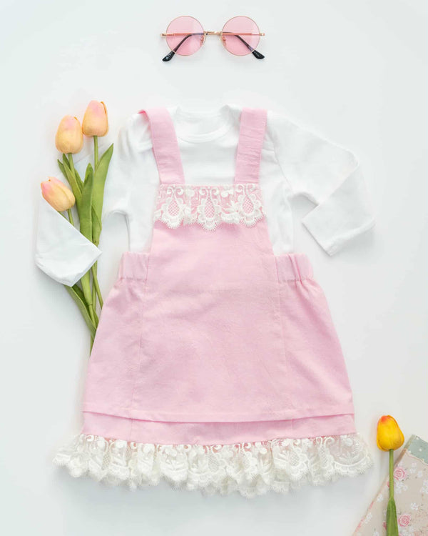 A pink dress with lace trim, white lace trim, and a white lace ruffle at the bottom, along with a pair of sunglasses and a bouquet of tulips, all arranged on a white background.