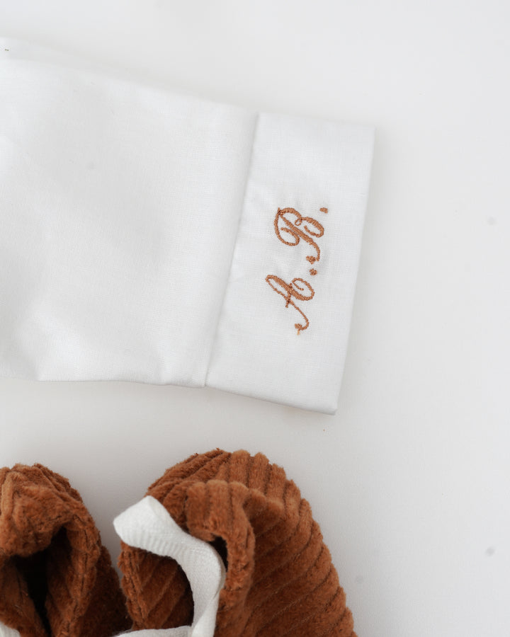 a white sleeve with a personalized embroidered text on it, and a brown corduroy item next to it.