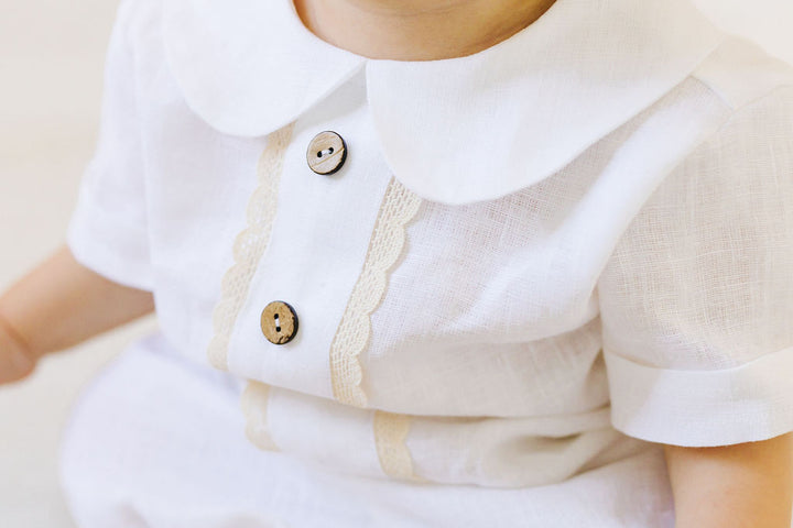 A close-up of a child's white dress with a scalloped collar and two buttons.