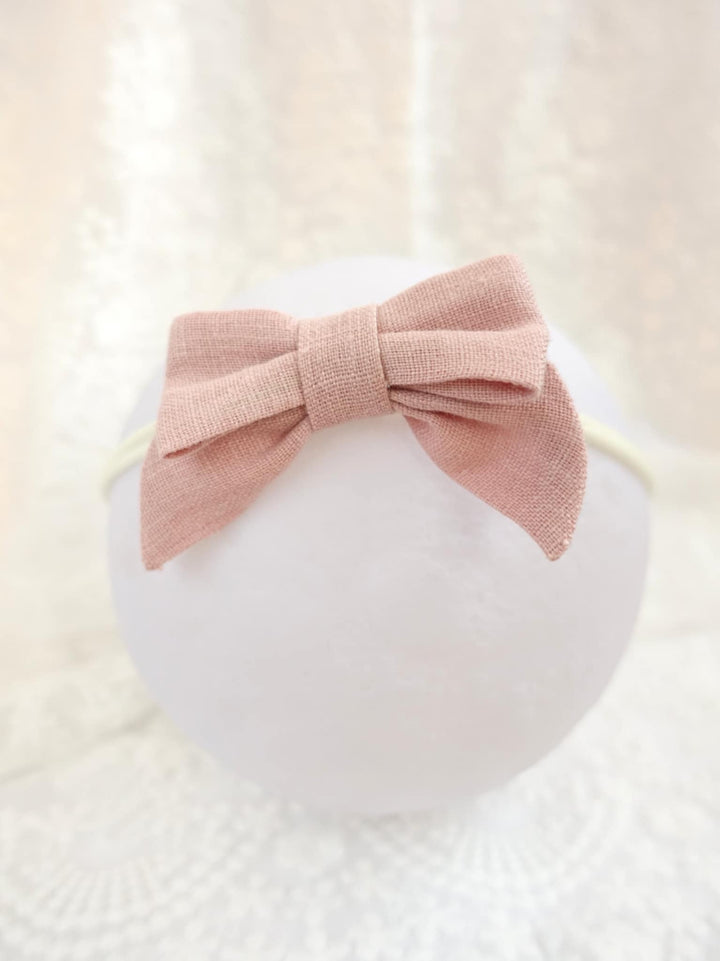 A pink bow tie is tied around a white headband, which is placed on a white lace background.