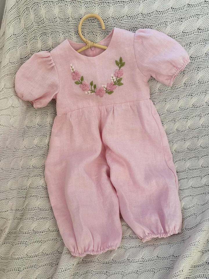 A pink, puffed-sleeved dress with a floral embroidered design on the front, hanging on a wooden hanger.